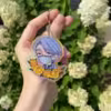 Portachiavi in acrilico con un personaggio anime dai capelli blu e una maschera, circondato da fiori.