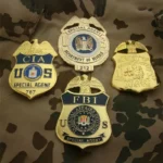 Vier verschiedene Abzeichen, darunter ein CIA-Abzeichen, auf einem Tarnungshintergrund.
