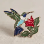 Enamel pin showcasing a hummingbird and flower, a delightful accessory for those who appreciate unique, nature-themed jewelry.