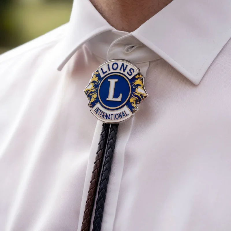 Ein Mann trägt eine blau-weiße Reversnadel, ergänzt durch eine Lion Club Bolo-Krawatte.