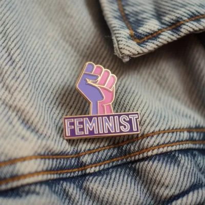 Épingle en émail portant le mot "Feminist" en lettres grasses, symbolisant le soutien aux droits des femmes et à l'égalité des sexes.